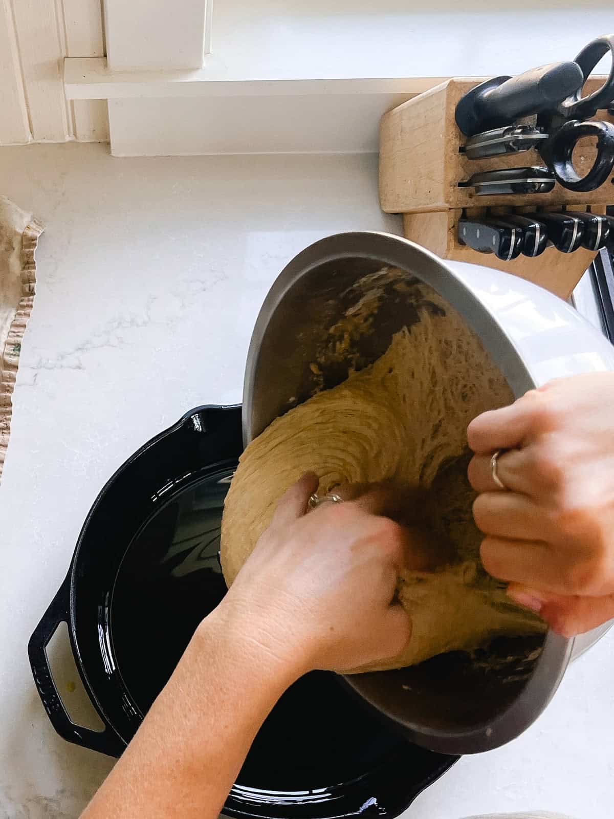 Transferring focaccia dough from a metal mixing bowl to a cast iron skillet.