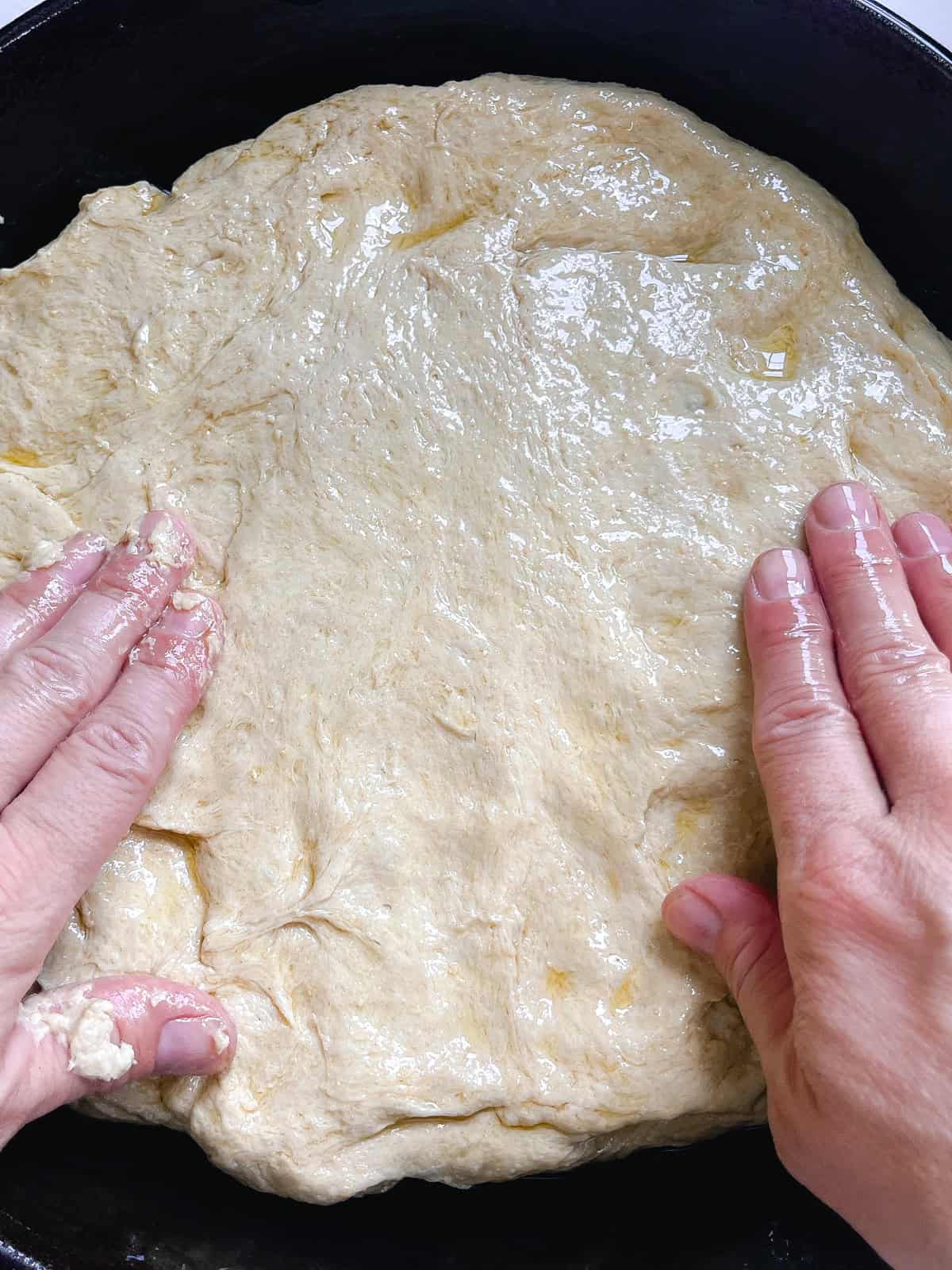 Pressing on focaccia dough to fit it to the cast iron skillet.