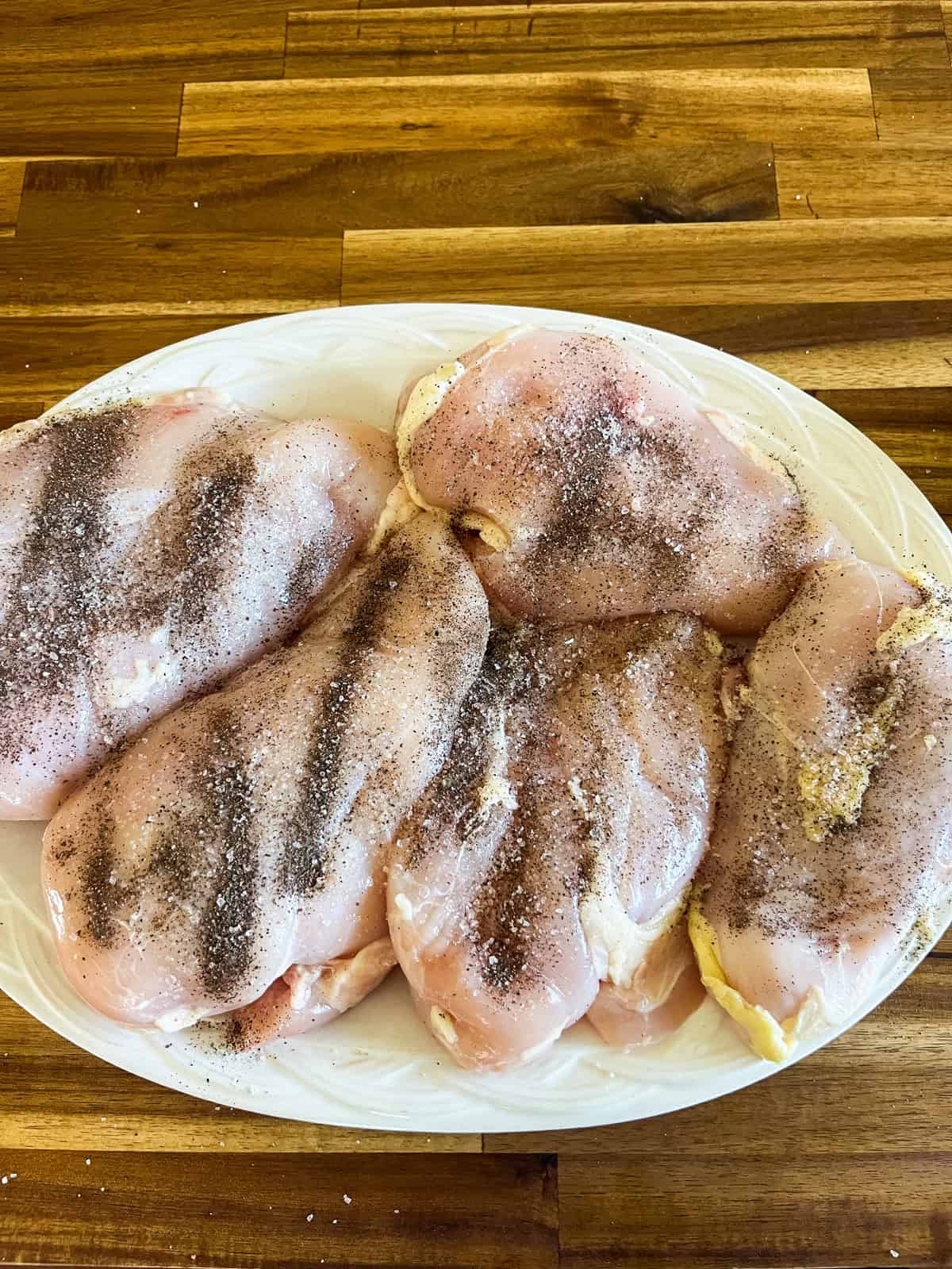 Seasoned raw chicken breasts sitting on a plate.