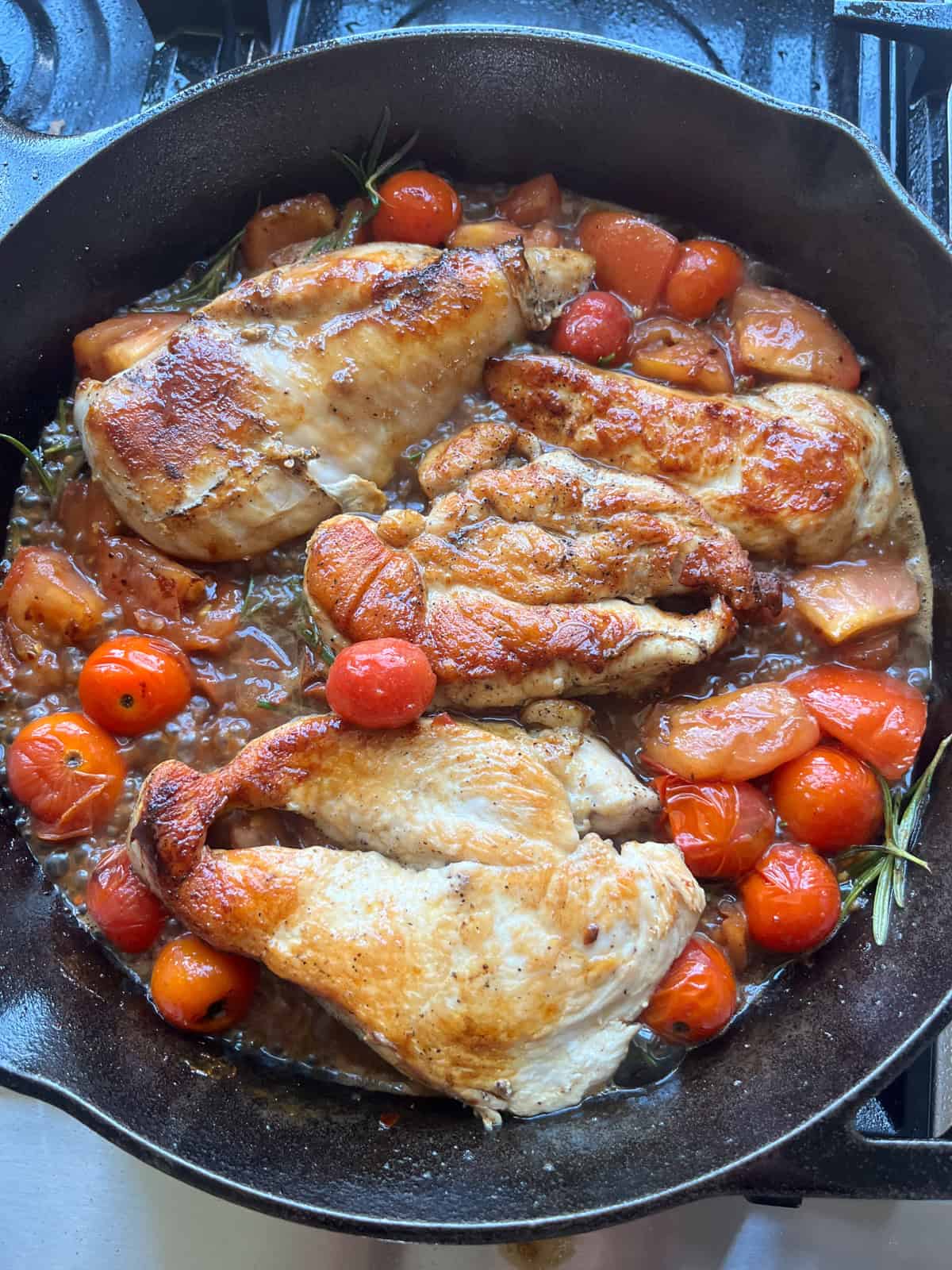Cherry tomatoes and chicken cutlets cooking togetehr in a cast iron skillet.