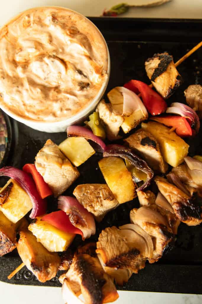 Hawaiian chicken kabobs on a serving tray with a bowl of chipotle cream sauce.