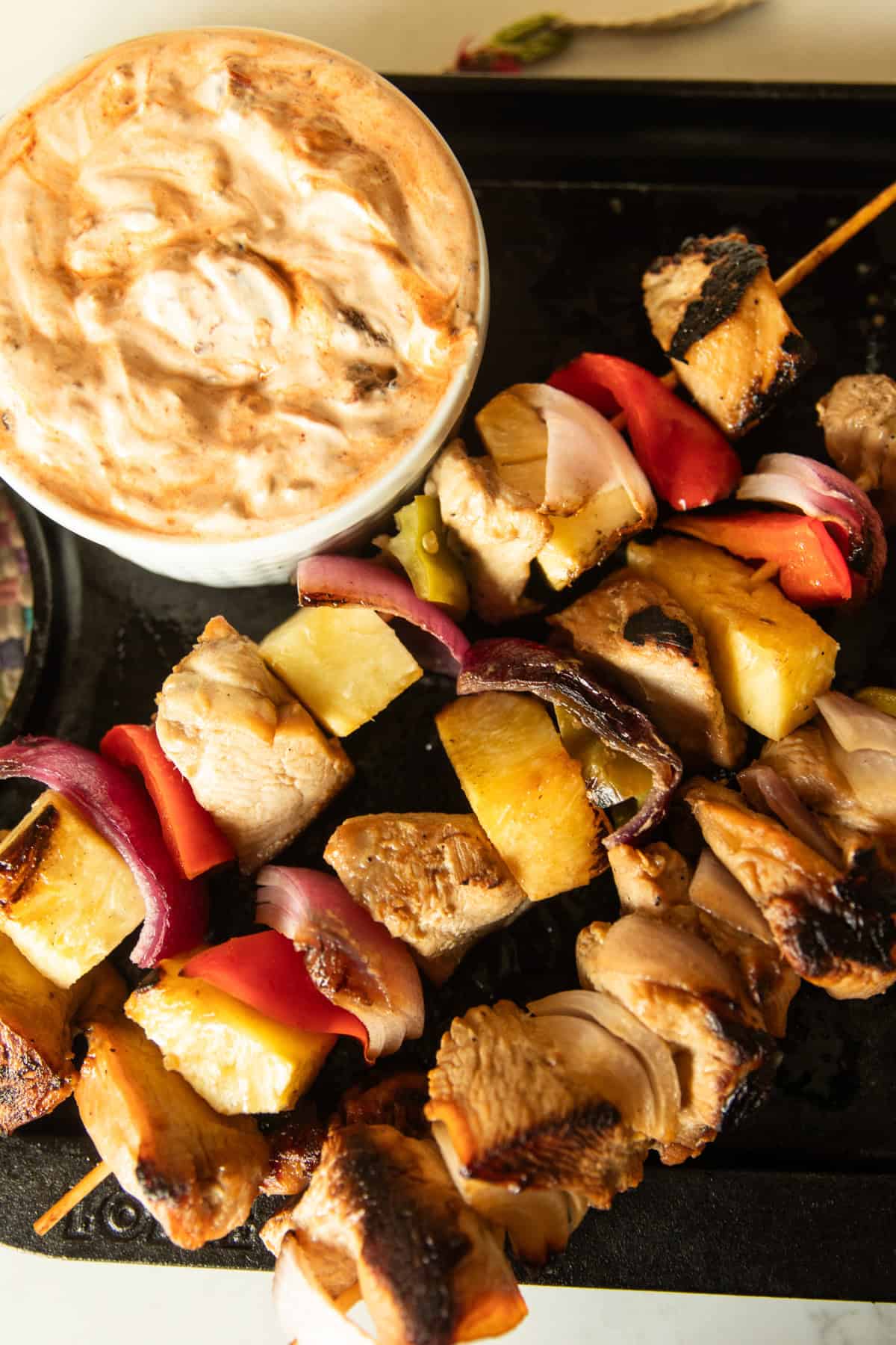 Hawaiian chicken kabobs on a serving tray with a bowl of chipotle cream sauce.