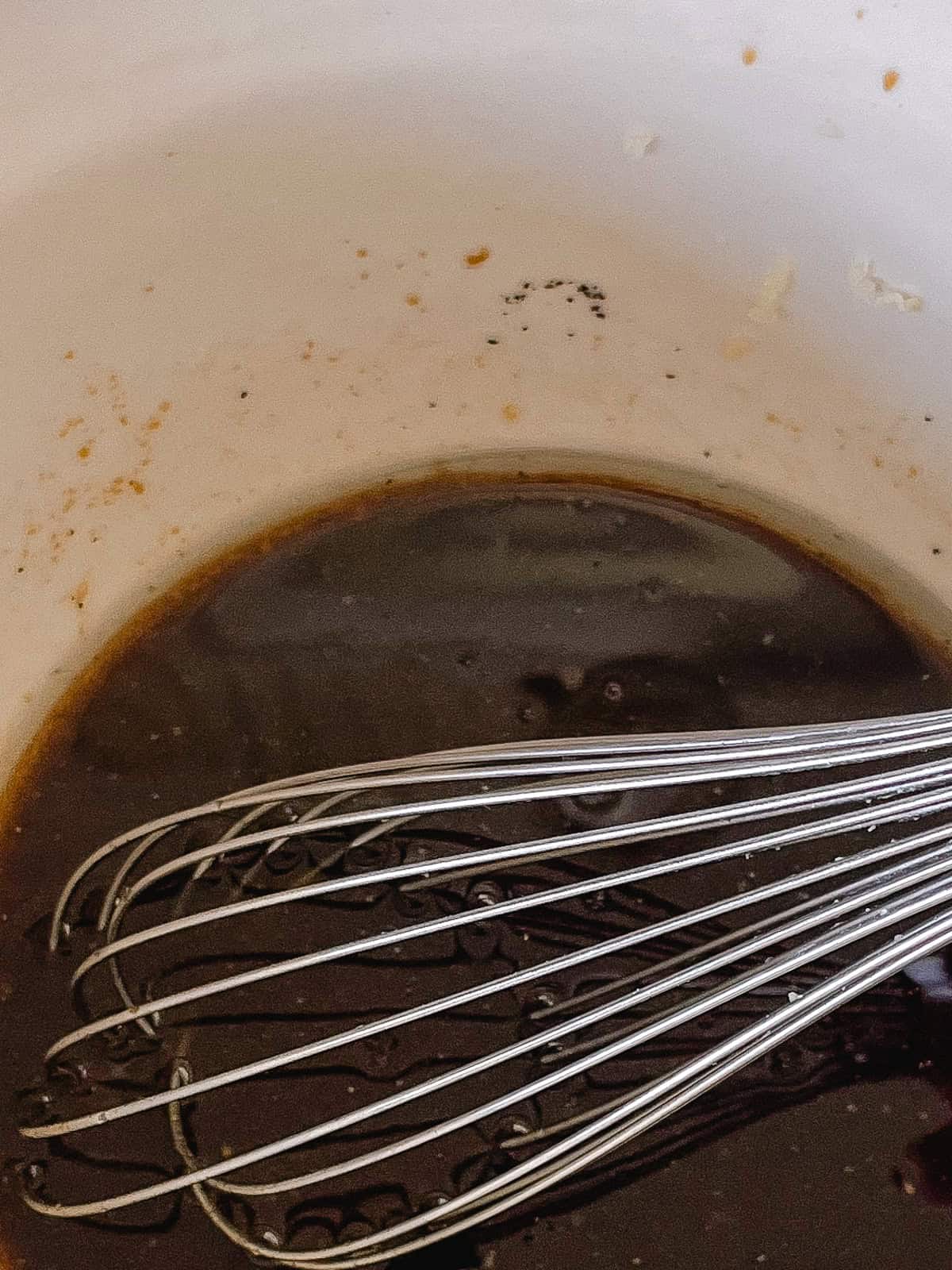 Whisking homemade marinade in a white mixing bowl.