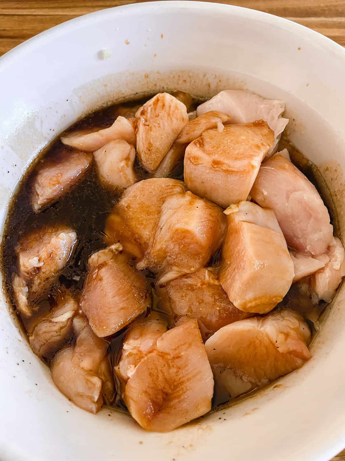 Cubed raw chicken in a bowl of marinade.