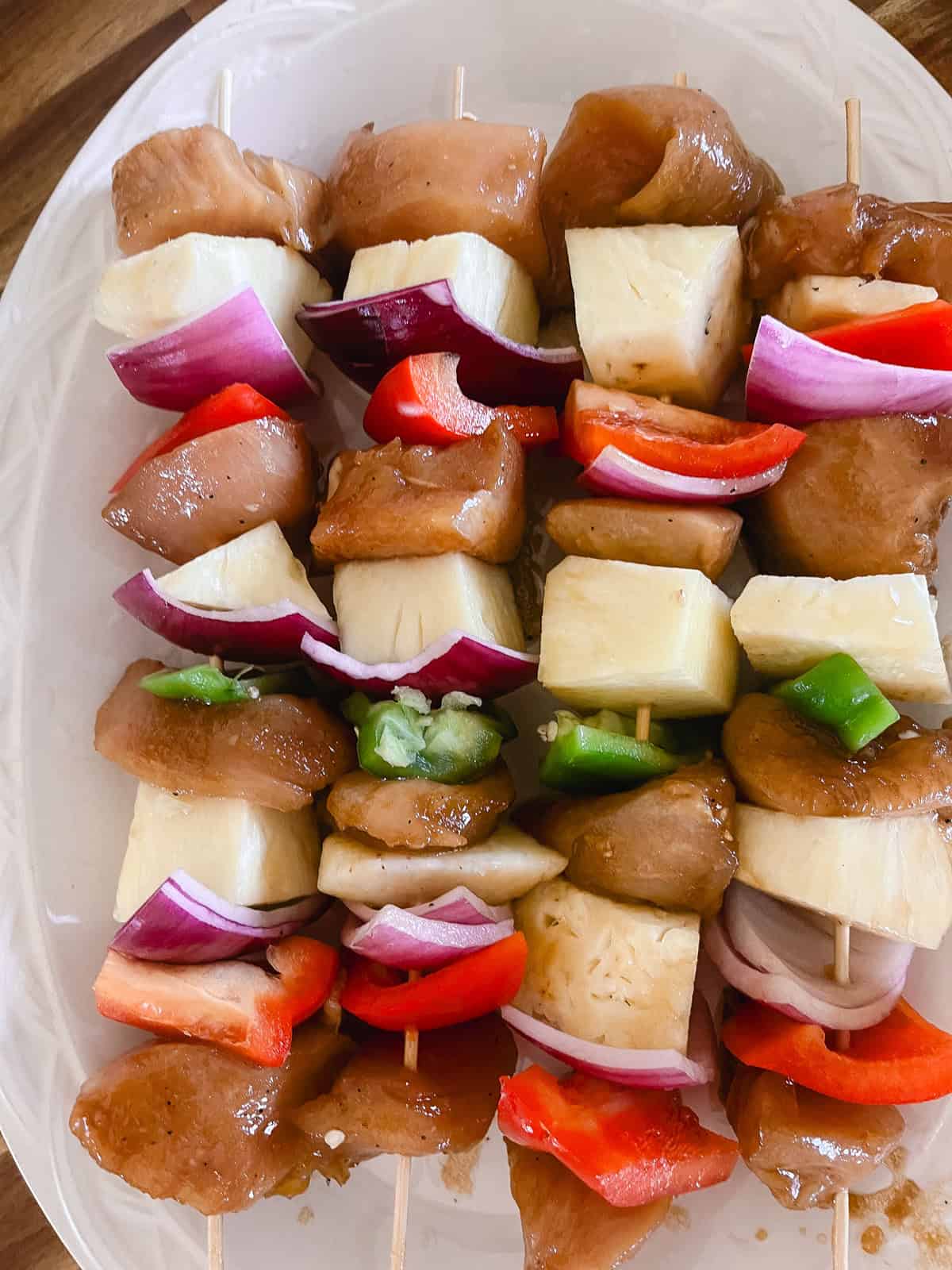 Uncooked kabobs on bamboo skewers lined up on a white platter.