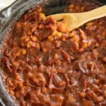 Bacon baked beans in a cast iron skillet with a wooden spoon.