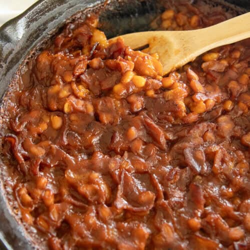 Bacon baked beans in a cast iron skillet with a wooden spoon.