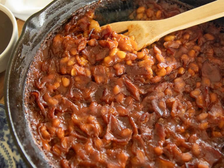 Bacon baked beans in a cast iron skillet with a wooden spoon.
