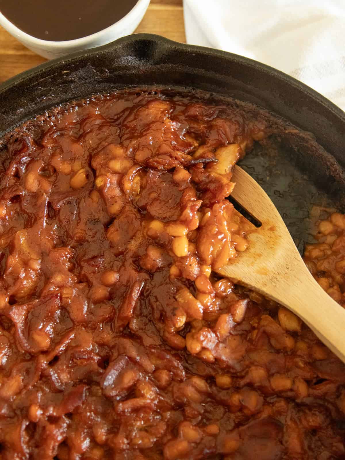 Bacon baked beans in a skillet with a wooden spoon.