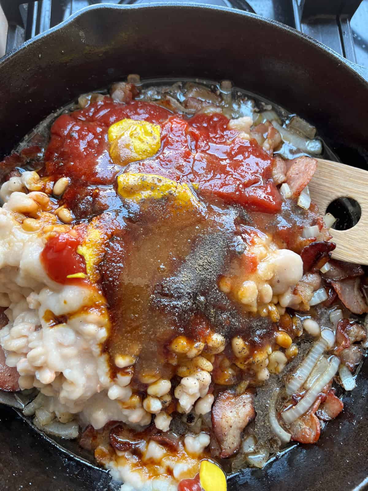 Bacon and onion in a skillet with ketchup, mustard, and other ingredients.