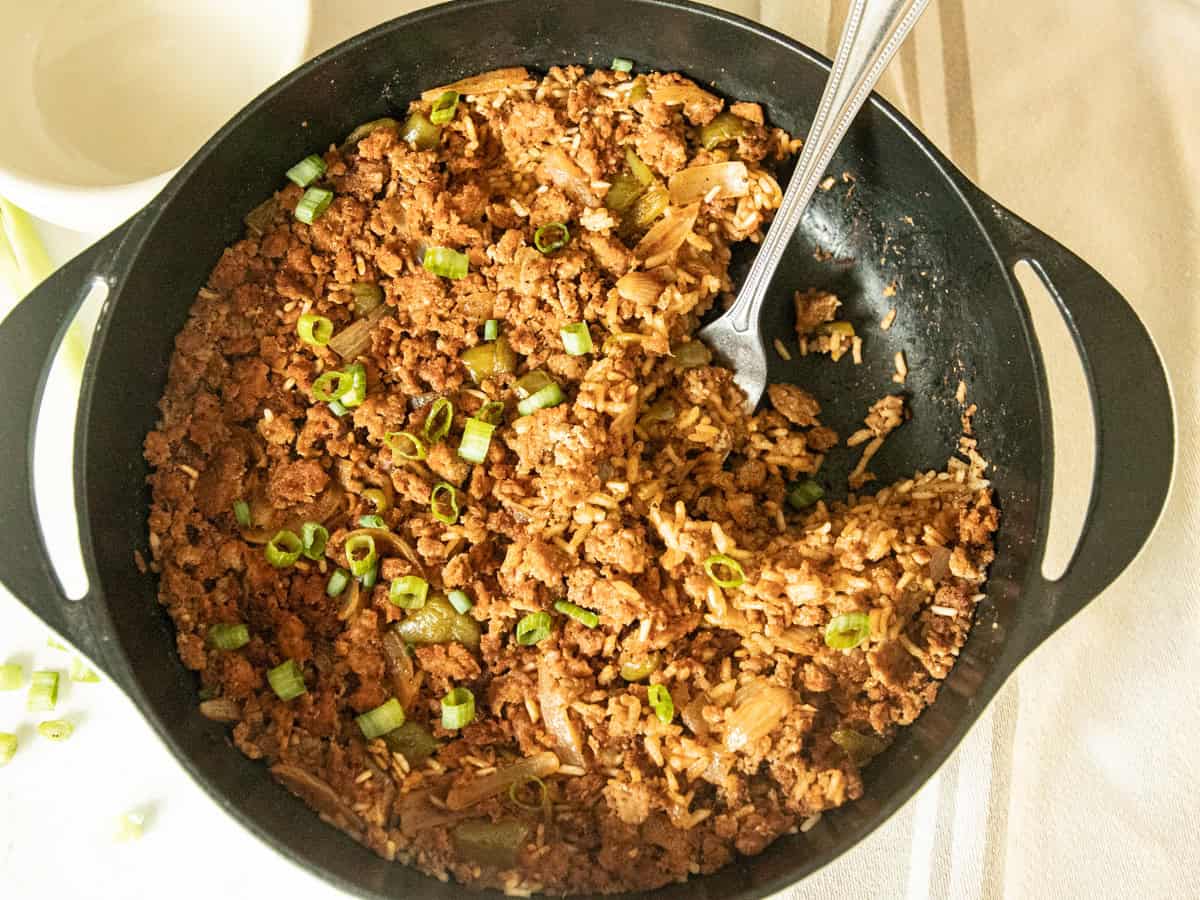 Scooping Cajun sausage and rice skillet out of a cast iron.