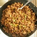A cast iron skillet with cajun sausage and rice and a fork.