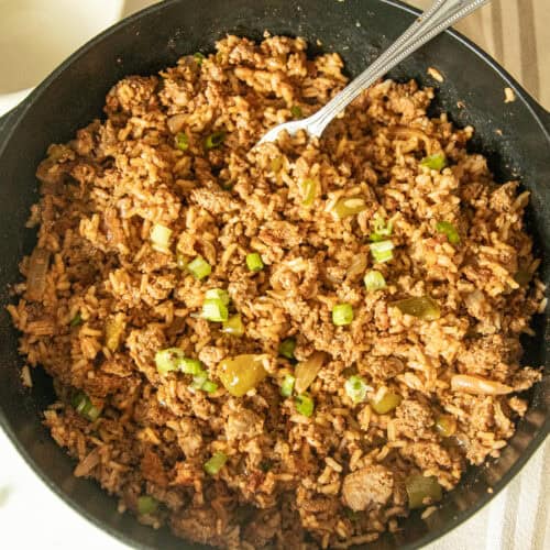 A cast iron skillet with cajun sausage and rice and a fork.