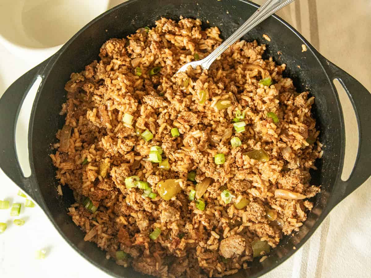 A cast iron skillet with cajun sausage and rice and a fork.