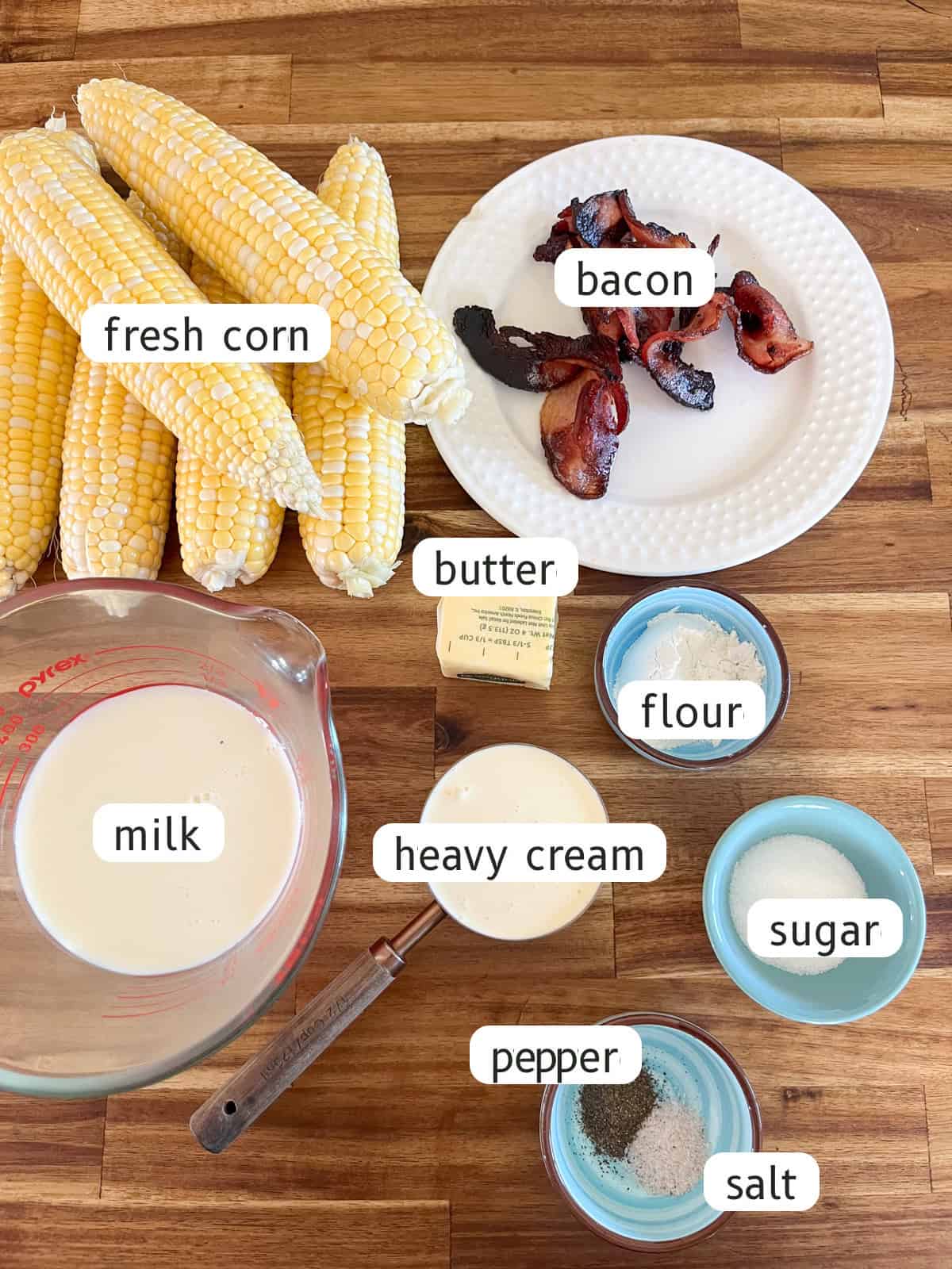 Cast iron skillet creamed corn ingredients labeled on a wooden table.