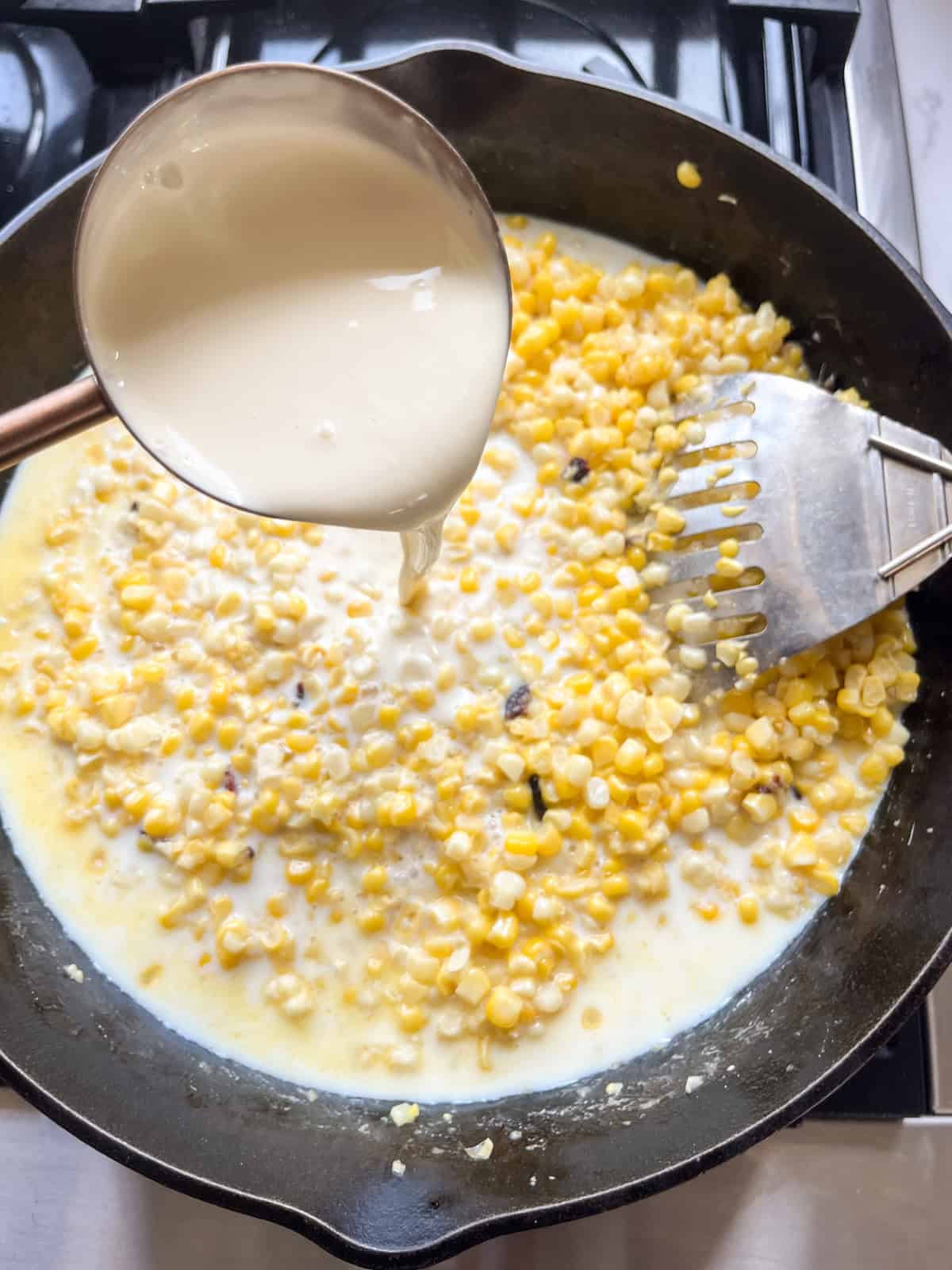 Pouring cream into a skillet of corn.