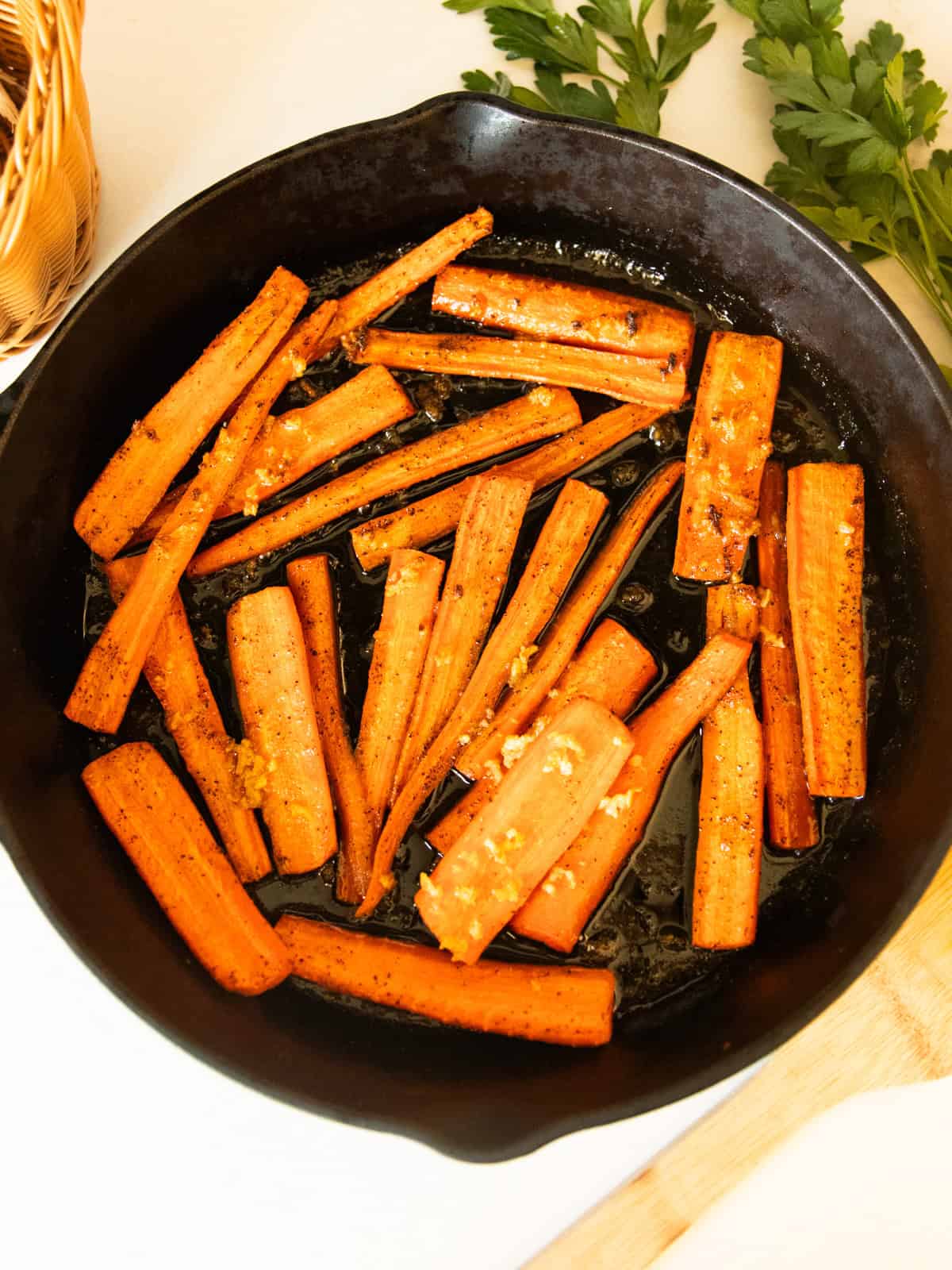 Cast iron glazed carrots in a skillet with fresh parsley to the side.