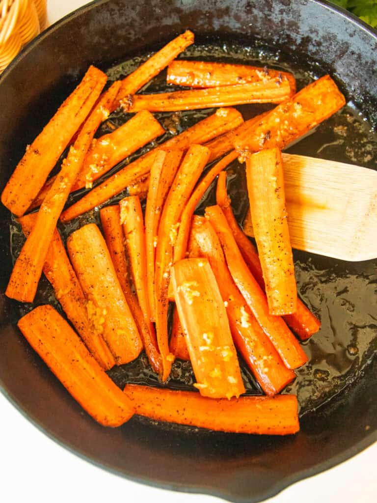 Scooping cast iron glazed carrots out of a skillet with a wooden spoon.