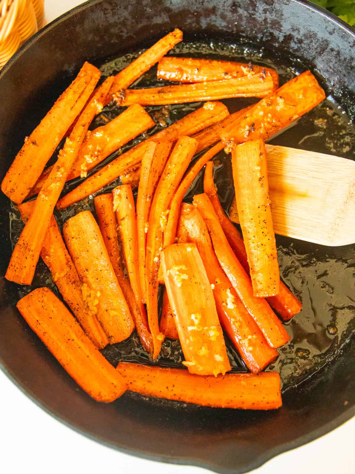 Scooping cast iron glazed carrots out of a skillet with a wooden spoon.