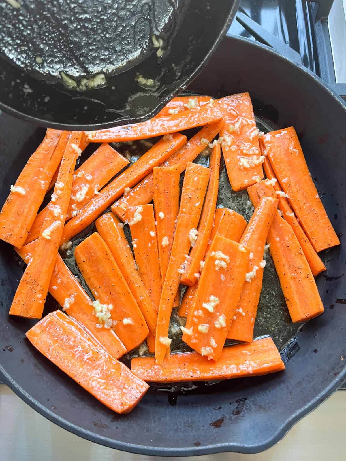 Drizzling glaze over carrots in a cast iron skillet.