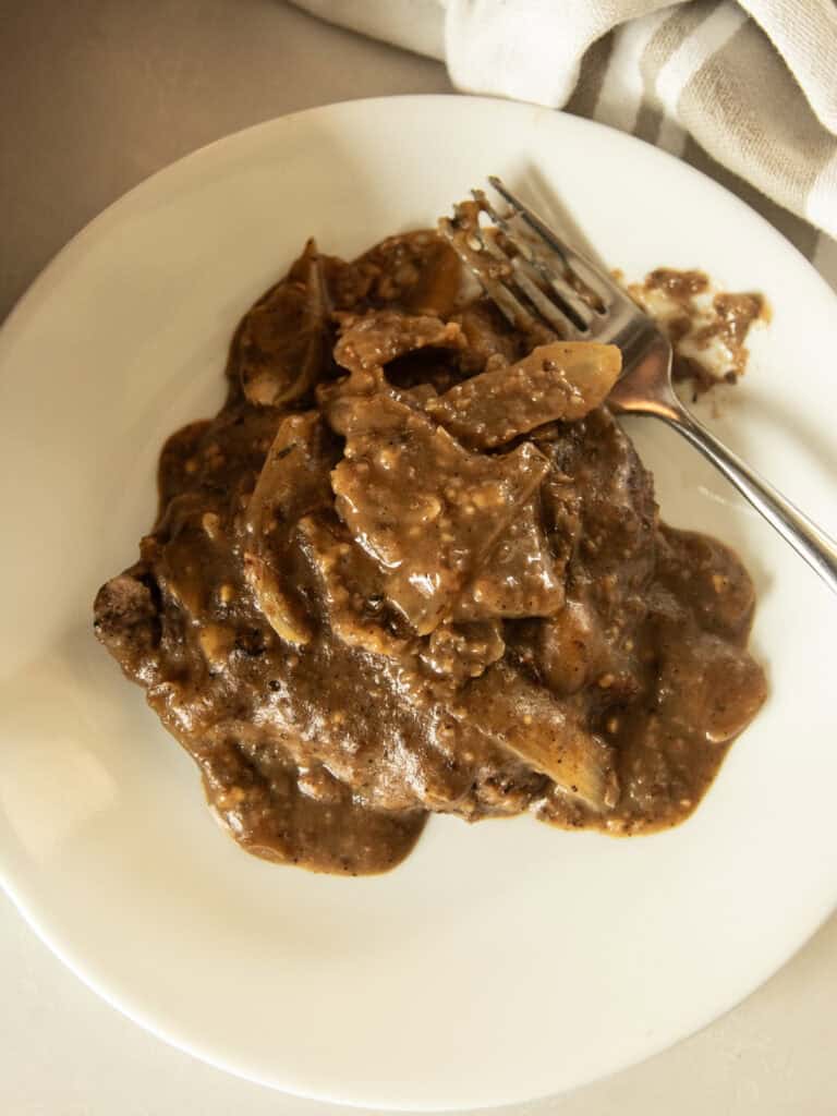 Cube steak and gravy on a white plate with a fork.