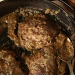 Cube steak and gravy cooking in a cast iron skillet.
