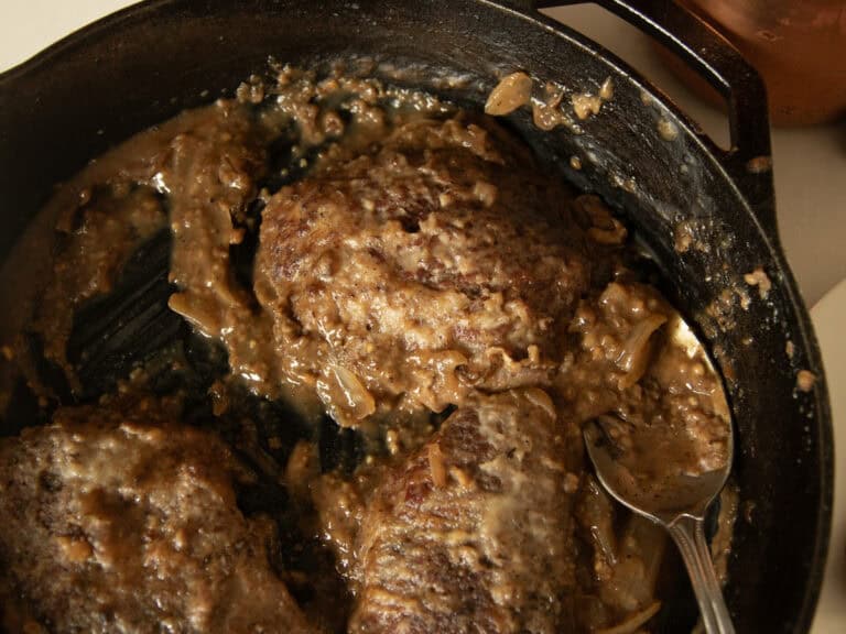 Cube steak and gravy cooking in a cast iron skillet.