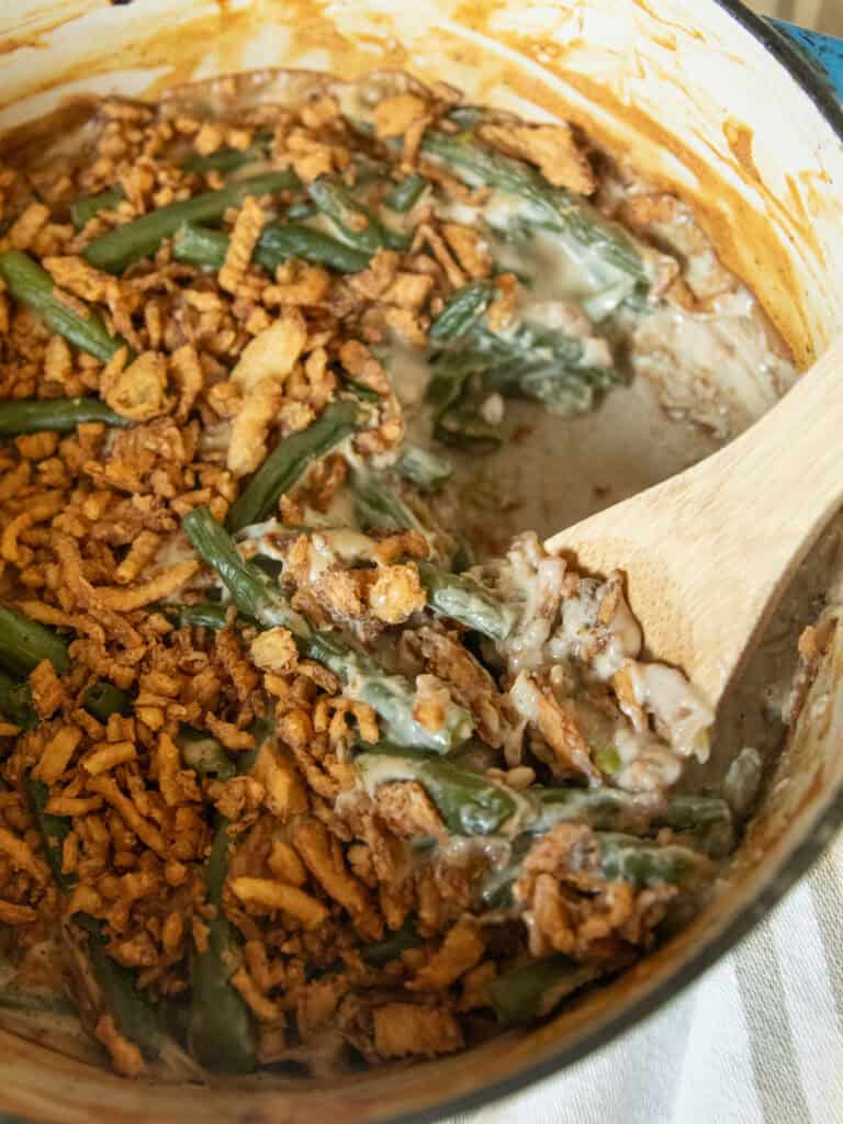 Scooping green bean casserole out of a dutch oven with a wooden spoon.