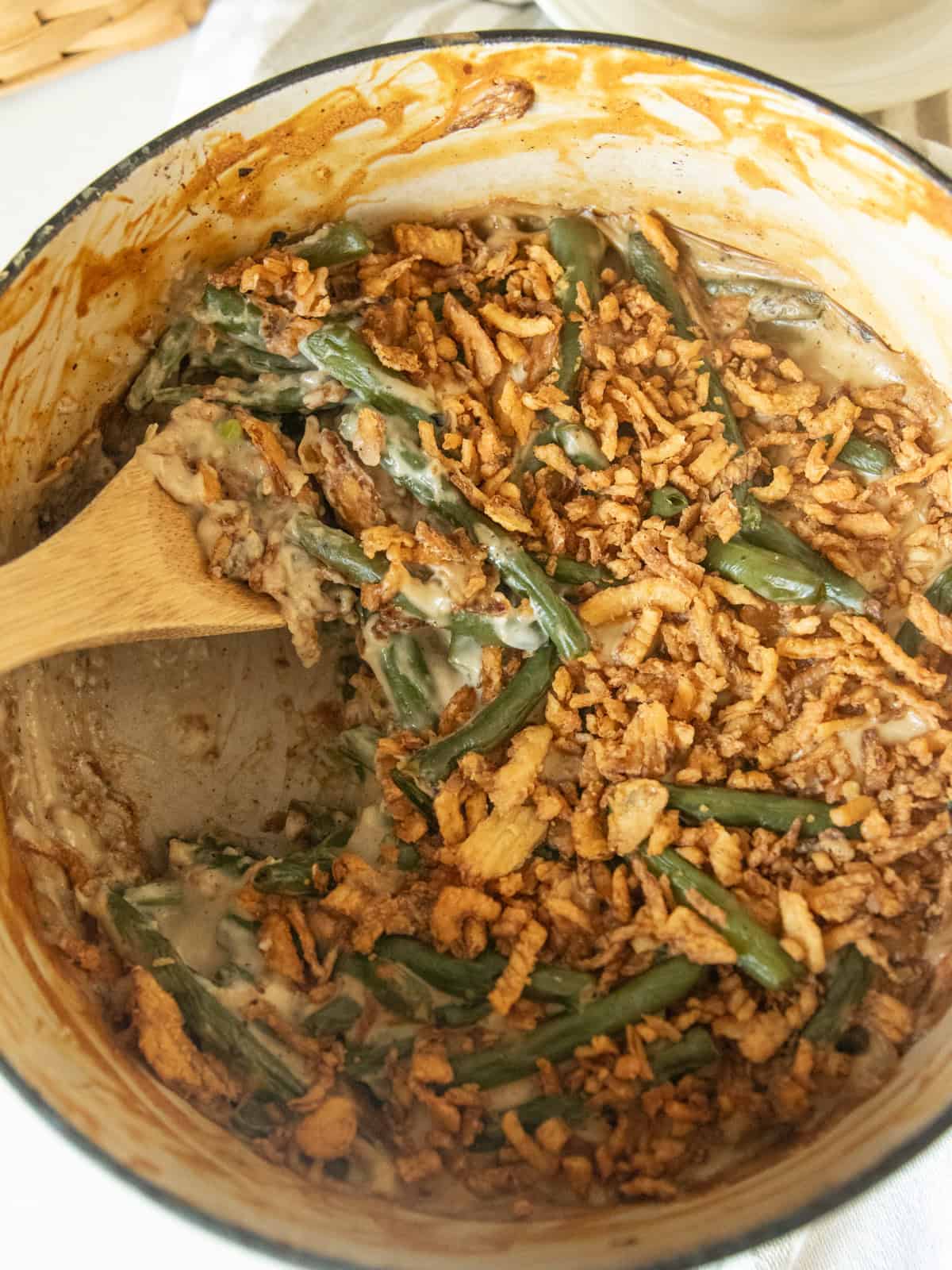 Scooping green bean casserole out of a Dutch oven with a wooden spoon.