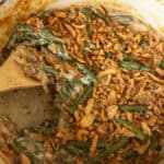 Scooping green bean casserole out of a dutch over with a wooden spoon.