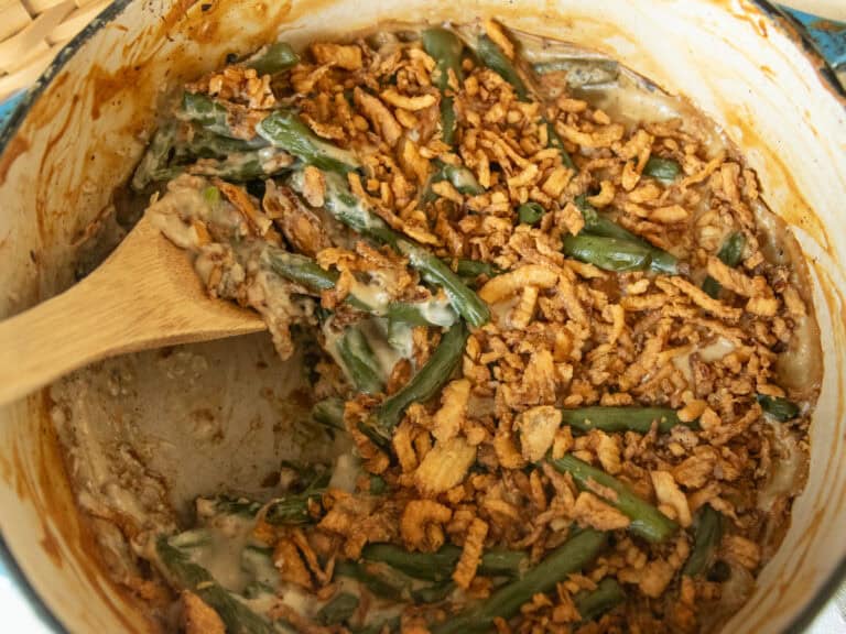 Scooping green bean casserole out of a dutch over with a wooden spoon.