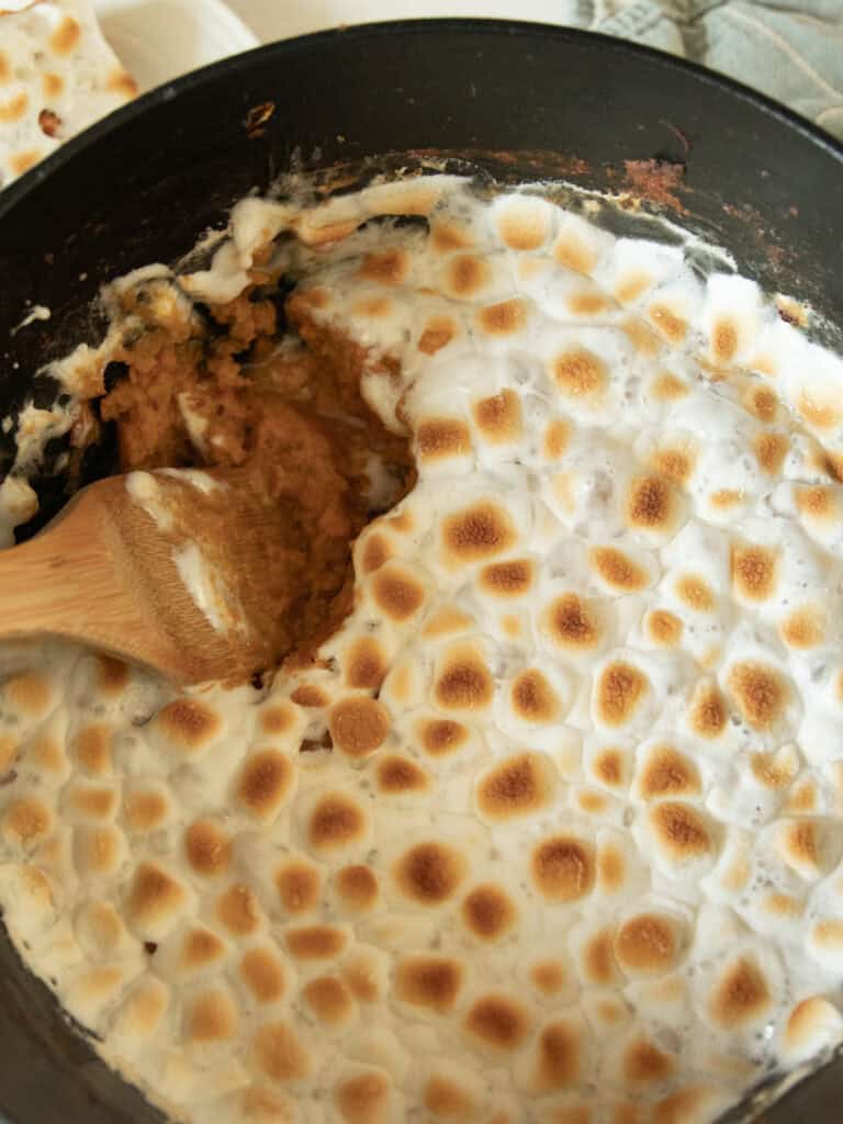 Scooping sweet potato casserole out of a Dutch oven with a wooden spoon.