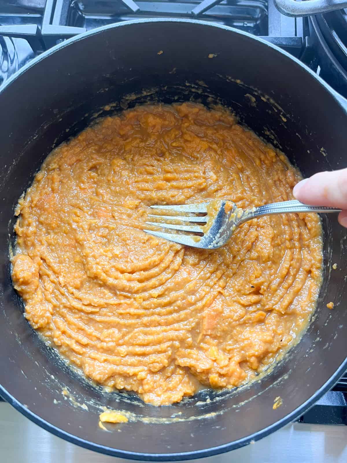 Smoothing the top of sweet potato casserole in a Dutch oven with a fork.