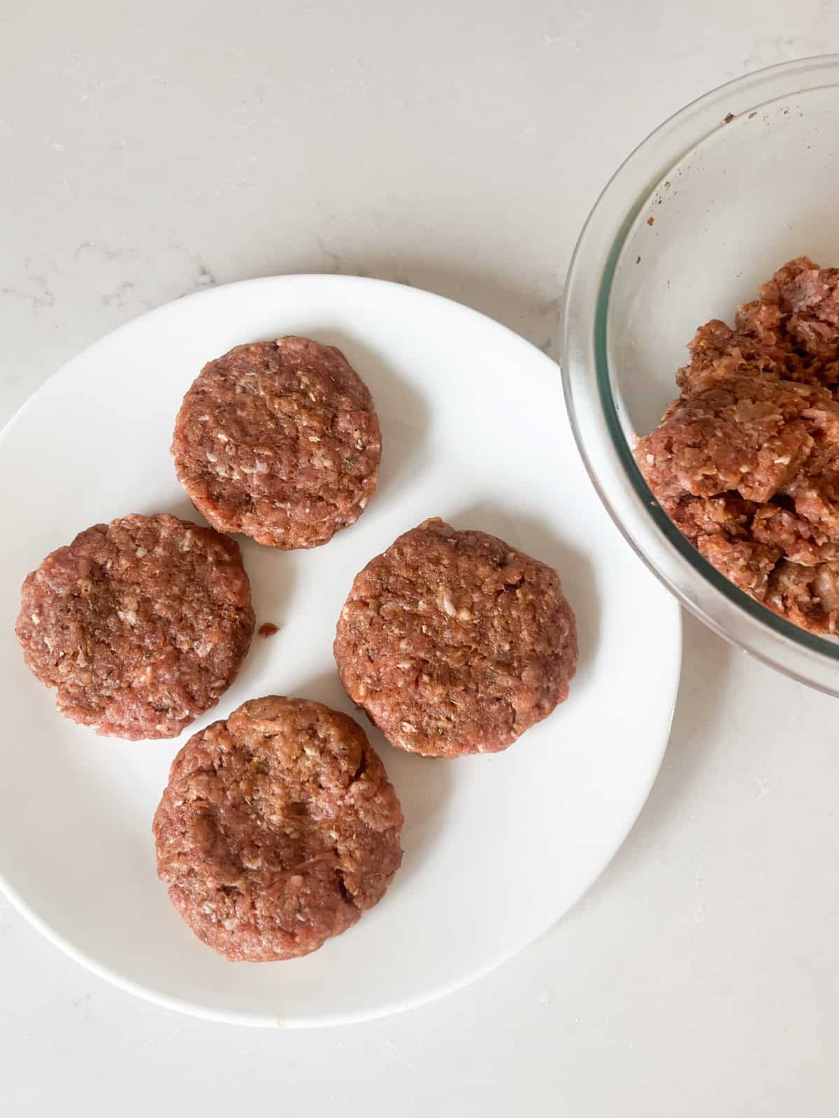 Raw homemade sausage patties on a white plate.