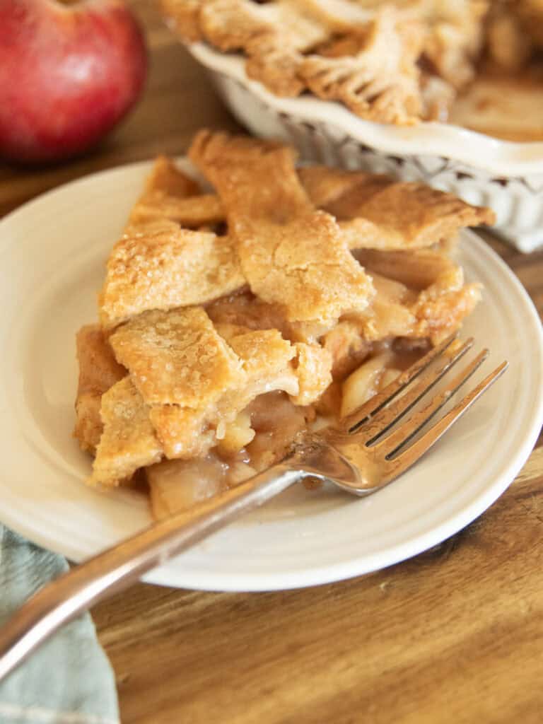 A slice of lattice apple pie with a whole pie in the background.