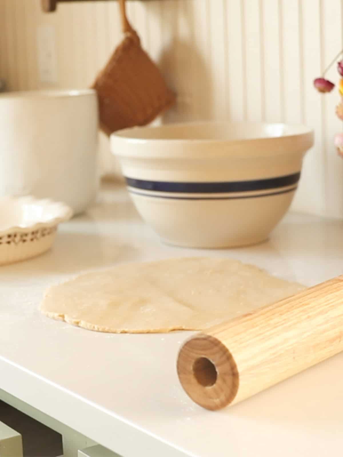 A pie crust unrolled on a kitchen counter with a rolling pin next to it.