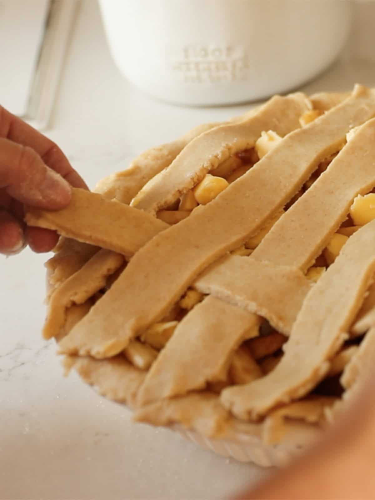 Weaving pie crust strips into a lattice pattern on top of the pie.