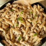 Creamy sausage pasta in a skillet with a wooden spoon.