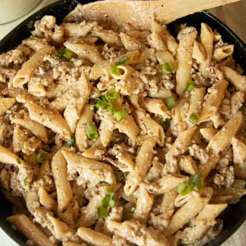 Creamy sausage pasta in a skillet with a wooden spoon.