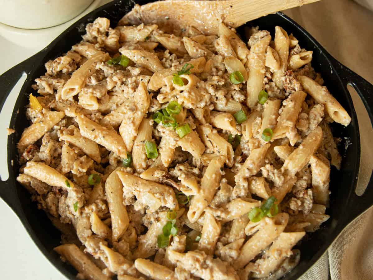 Creamy sausage pasta in a skillet with a wooden spoon.