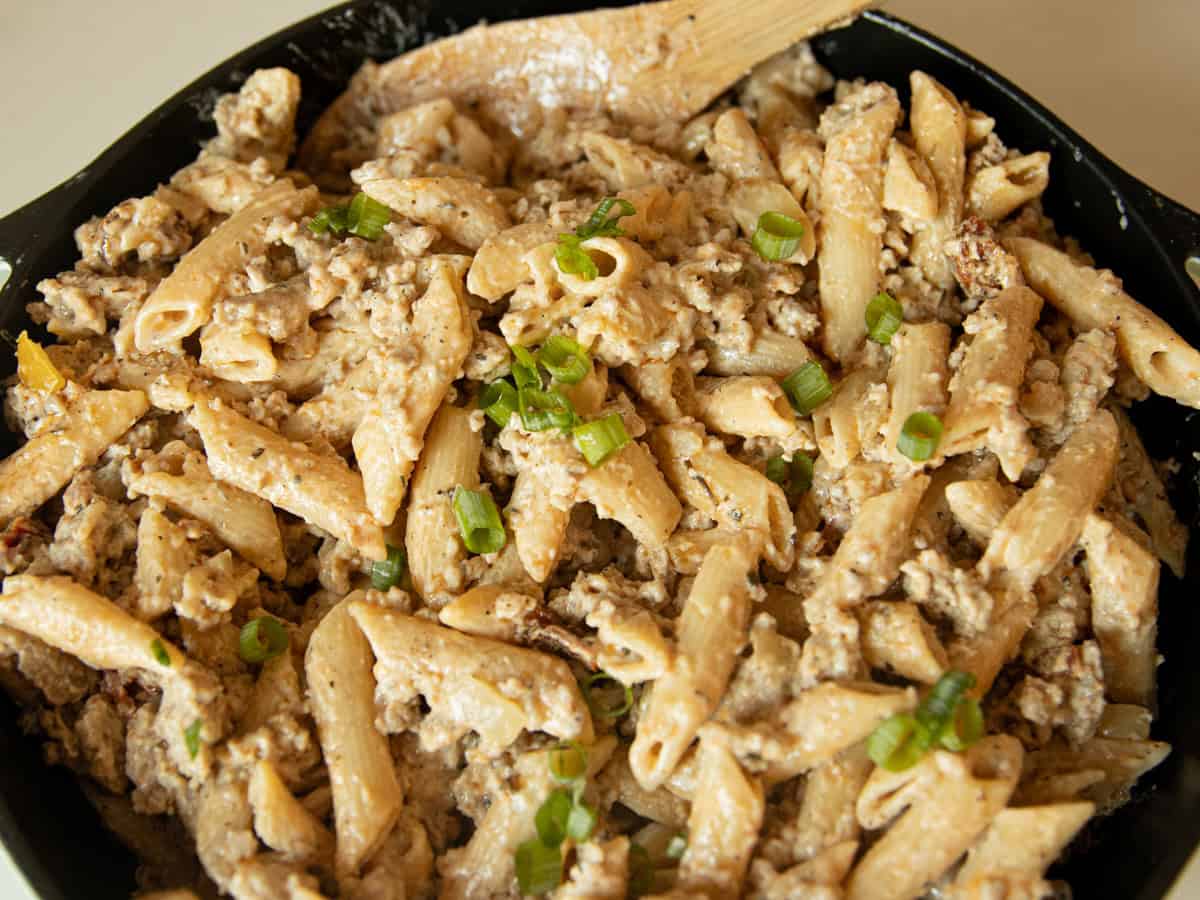 Creamy sausage pasta right before serving in a cast iron skillet with a spoon.