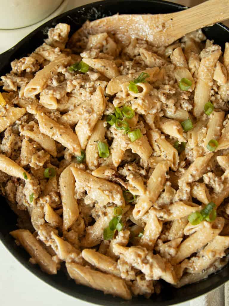 Creamy sausage pasta in a cast iron skillet with a wooden spoon.