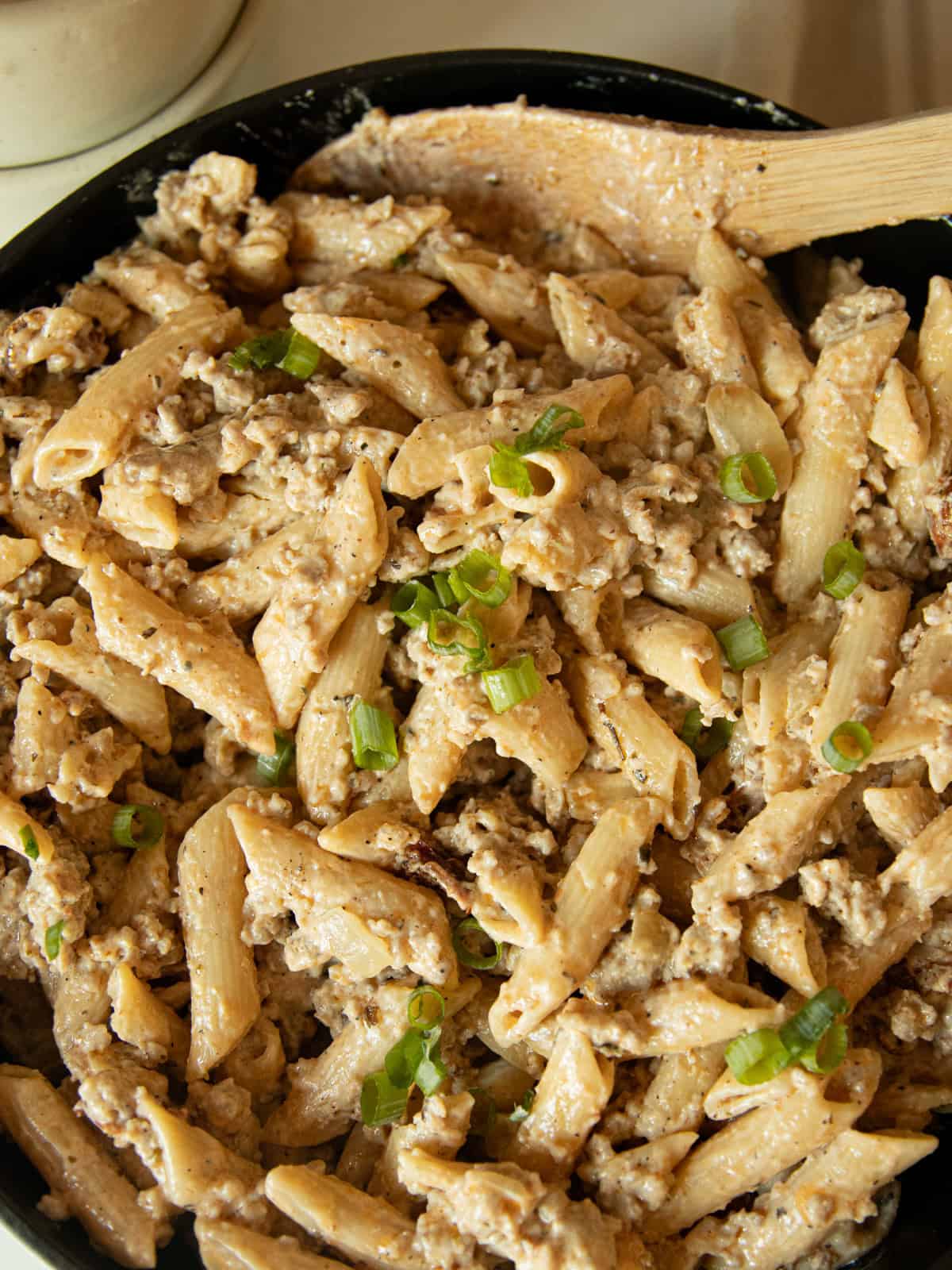 Creamy sausage pasta in a skillet with a spoon.