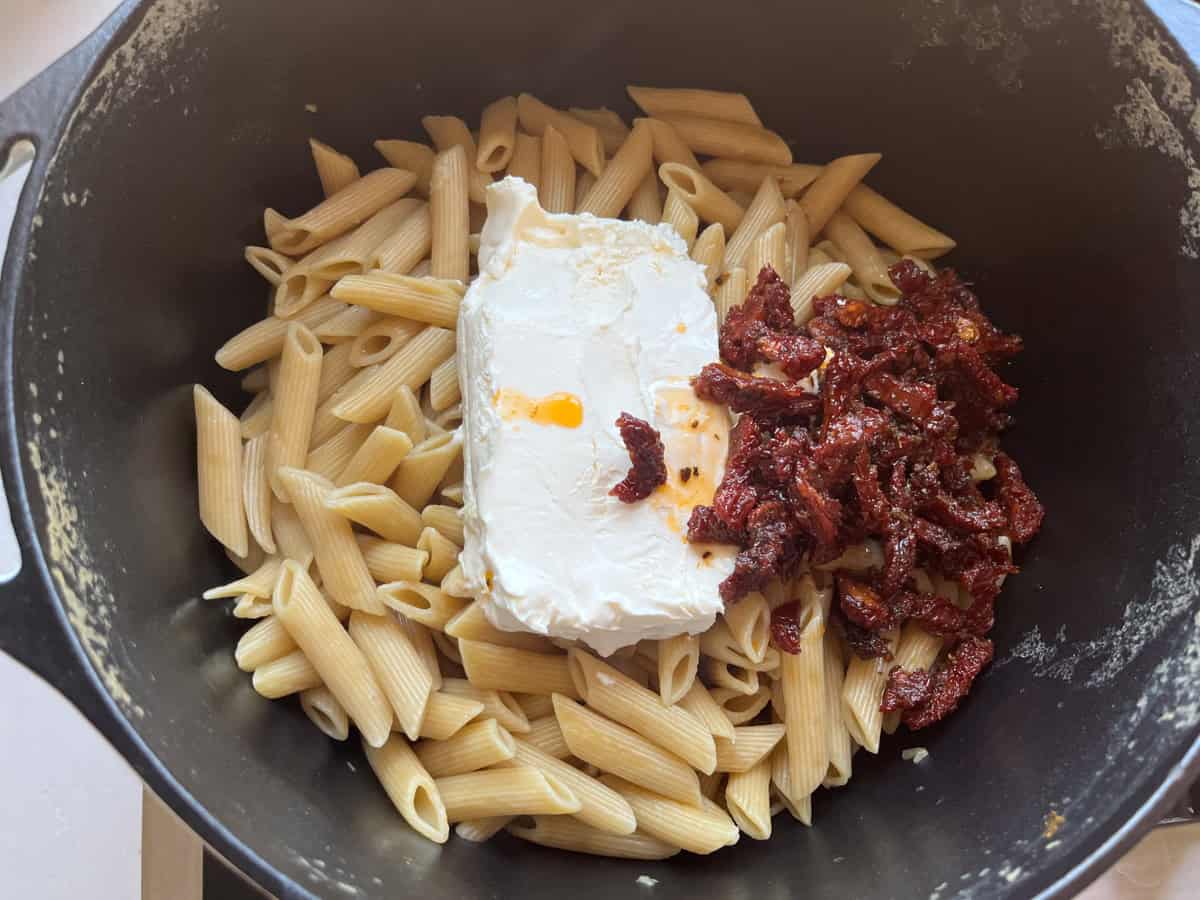Cooked pasta in a pan with sundried tomatoes and cream cheese.