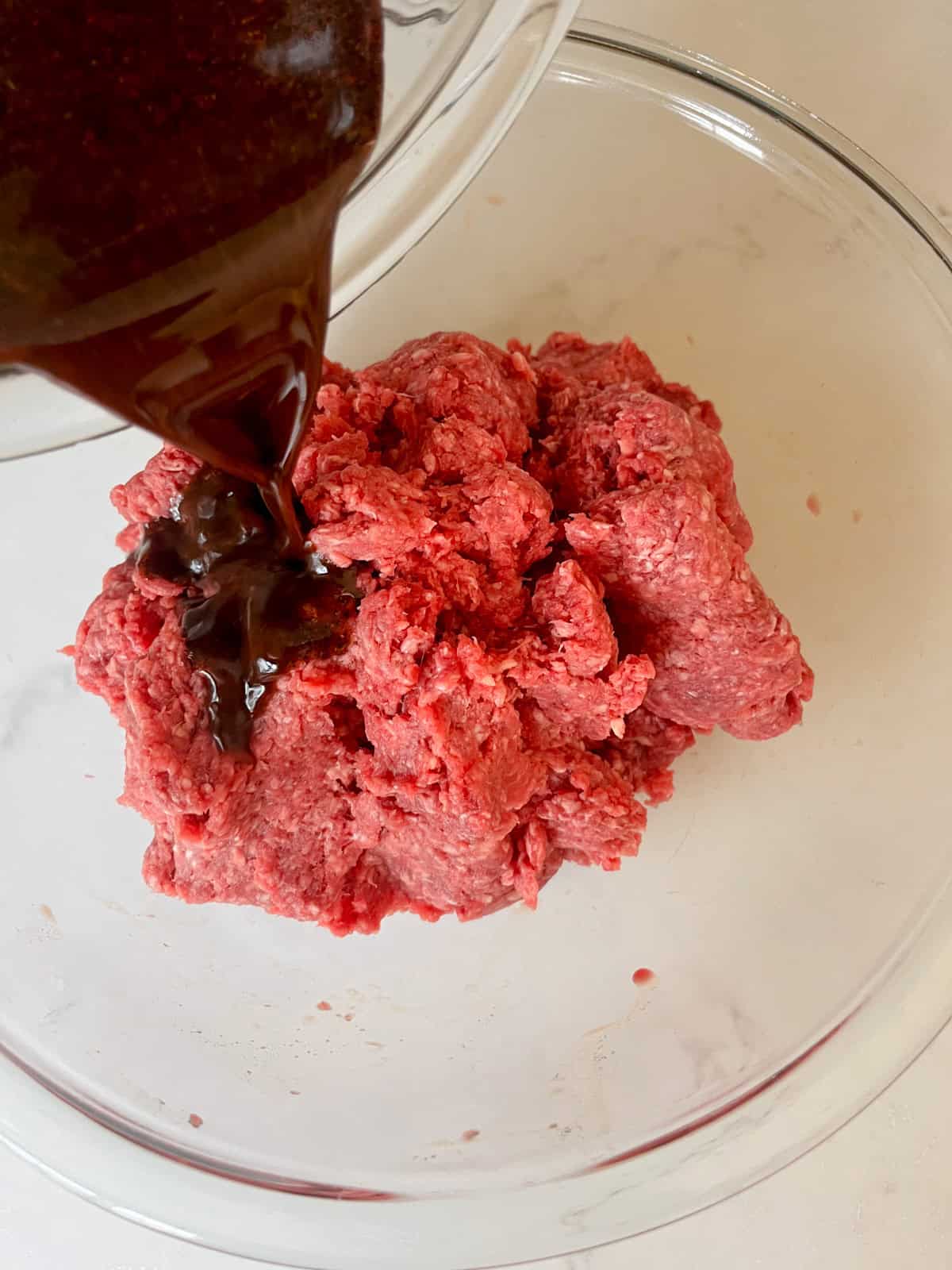Pouring seasoning mix over ground venison in a bowl.