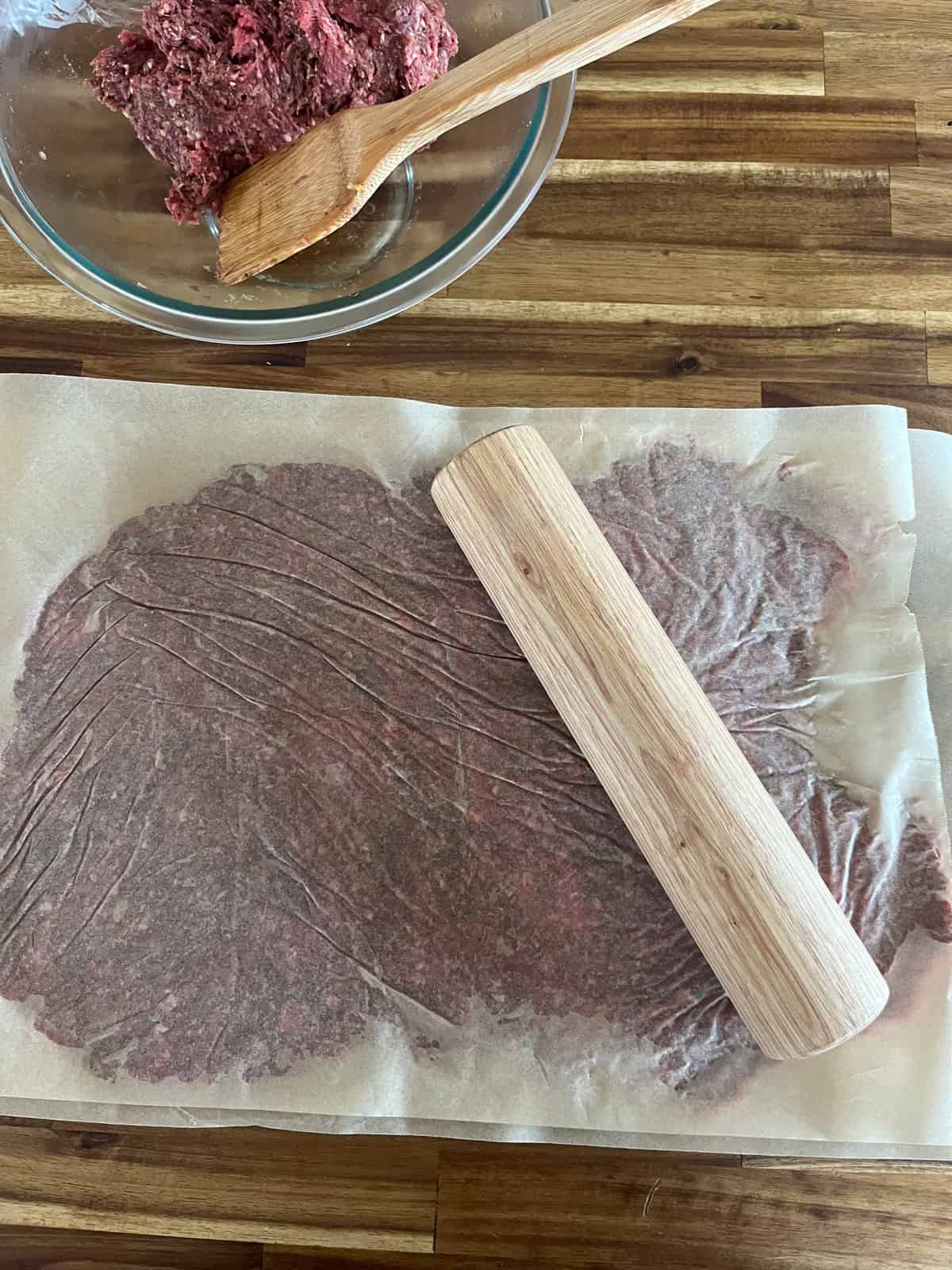 Ground venison in between two parchment sheets with a rolling pin.