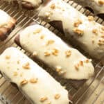 Maple bars with white glaze and walnuts lined up on a cooling rack.