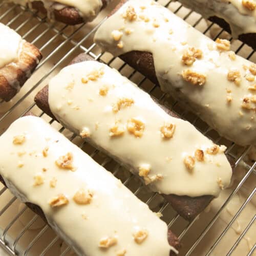 Maple bars with white glaze and walnuts lined up on a cooling rack.