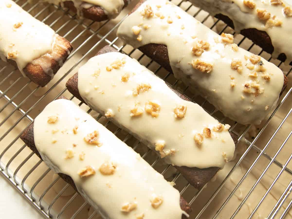 Maple bars with white glaze and walnuts lined up on a cooling rack.
