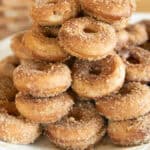 A stack of apple cider donuts on a white serving plate.